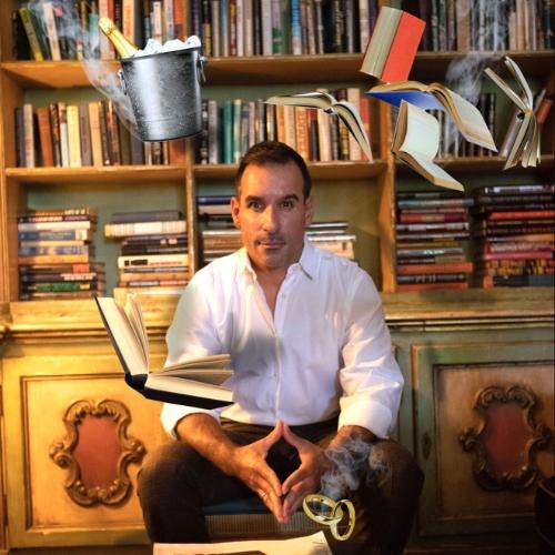 Man sitting in front of a bookshelf with floating books, rings, and a bucket all surrounding him